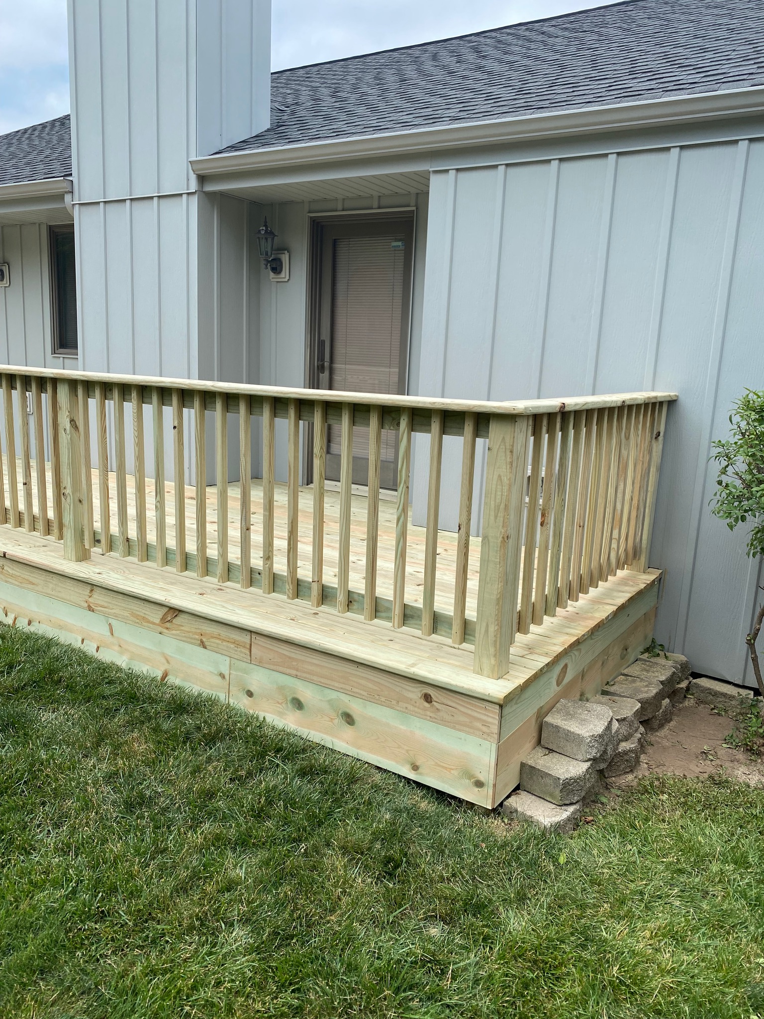 Custom pressure-treated wood deck platform with railings built along a grey residential home by Precision Exterior Inc.