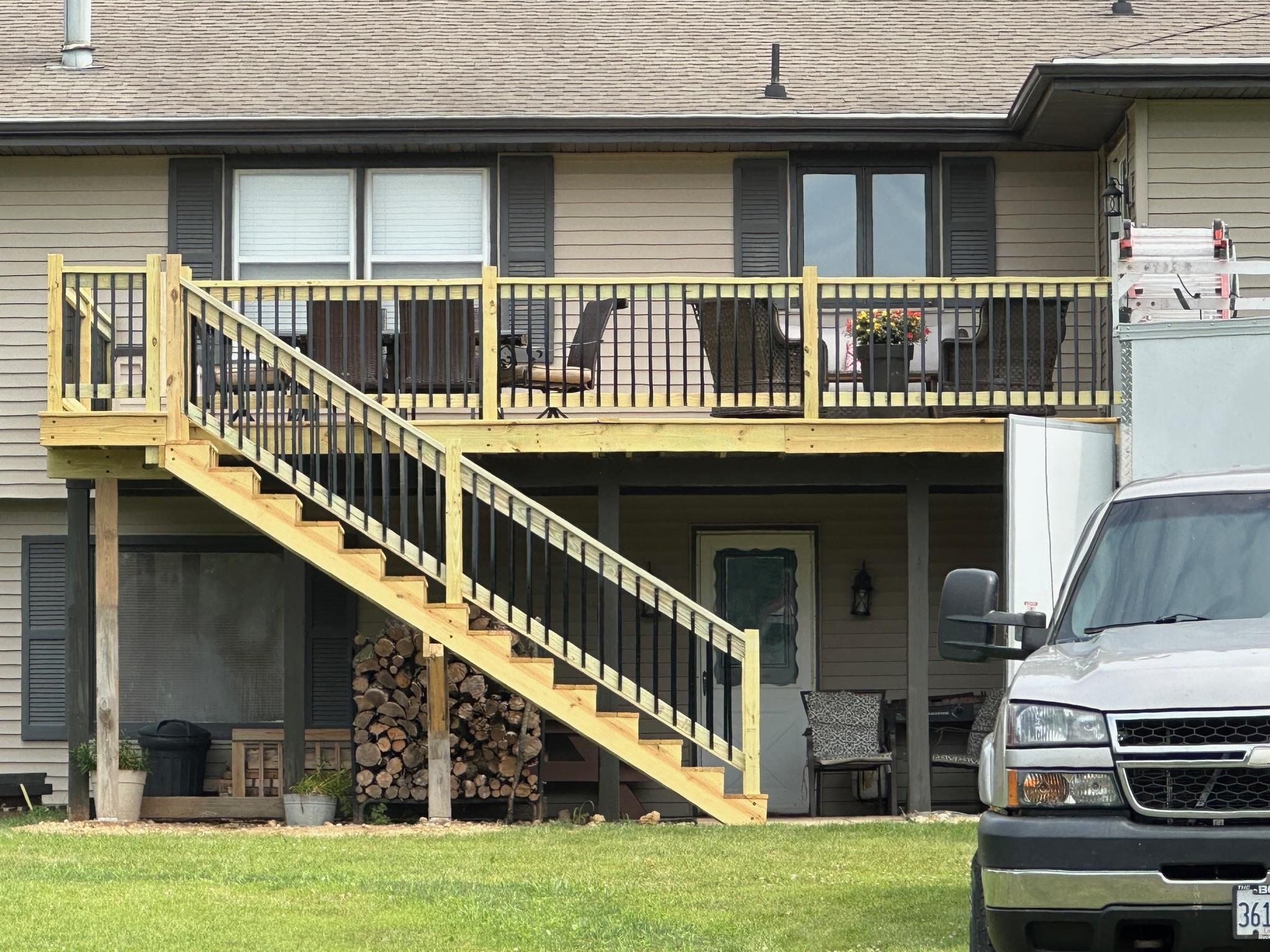 Elevated pressure-treated wood deck with an attached staircase and black metal balusters built on a residential home by Precision Exterior Inc.