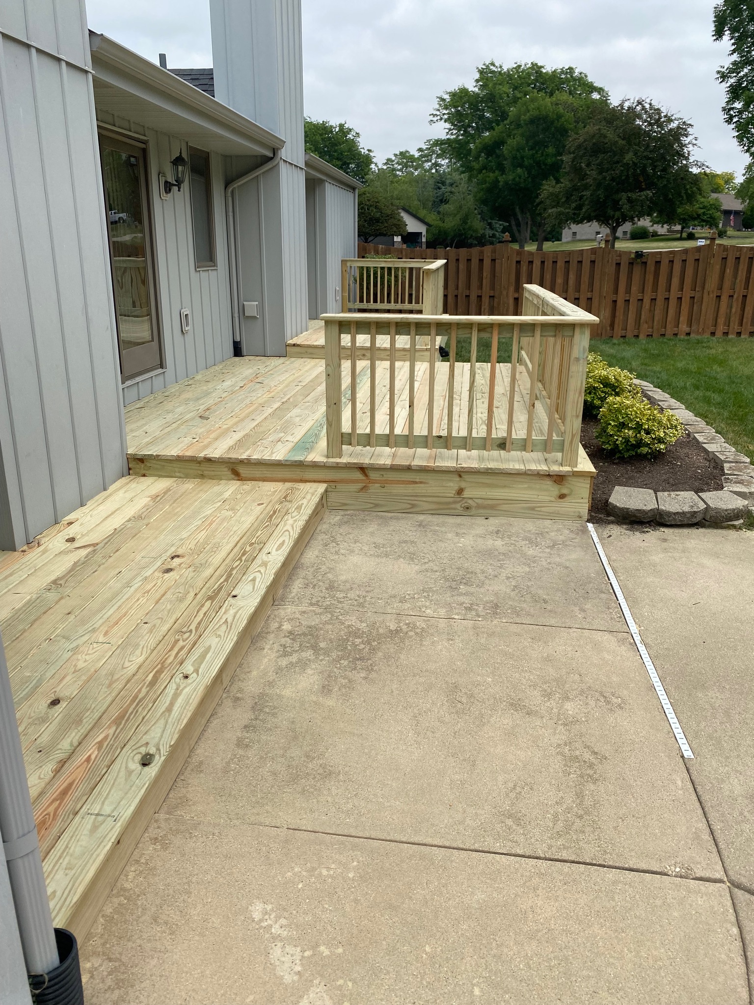 Newly constructed multi-level backyard wood deck with railings built next to a concrete patio by Precision Exterior Inc.