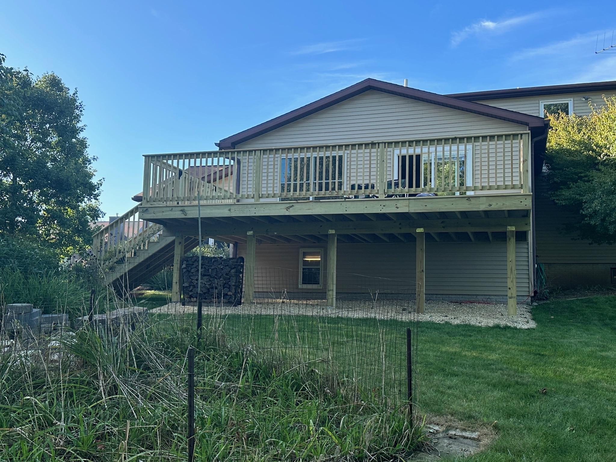 Large elevated backyard pressure-treated wood deck with stairs and safety railings built on a beige house by Precision Exterior Inc.