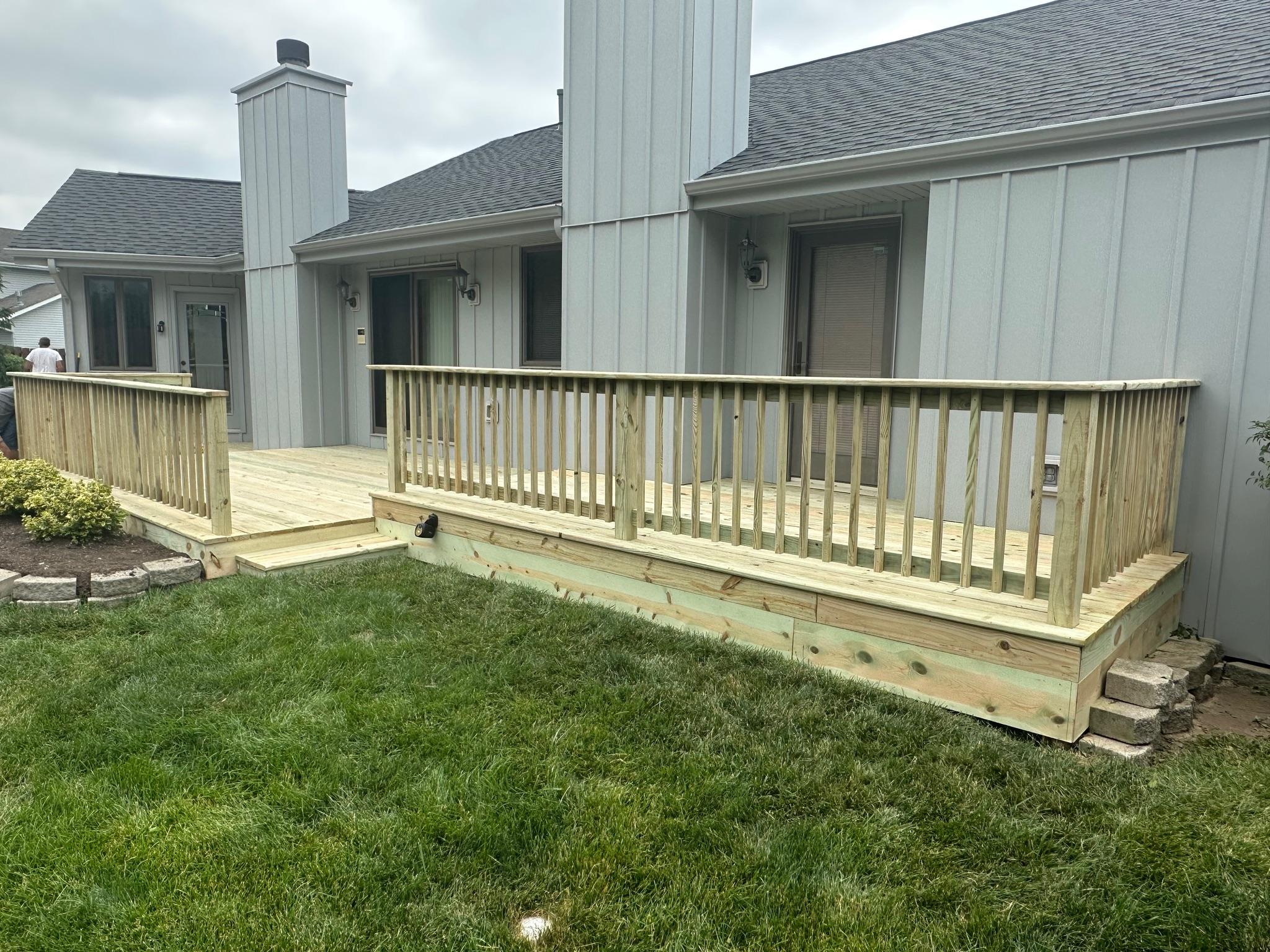 Newly constructed multi-level backyard wood deck with railings built on a grey house by Precision Exterior Inc.