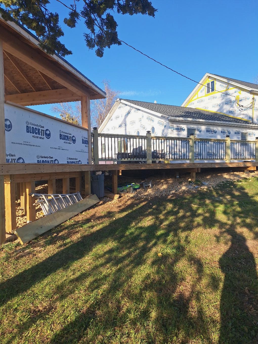 Custom residential wood deck construction with attached pavilion framing and black metal balustrade railings by Precision Exterior Inc.