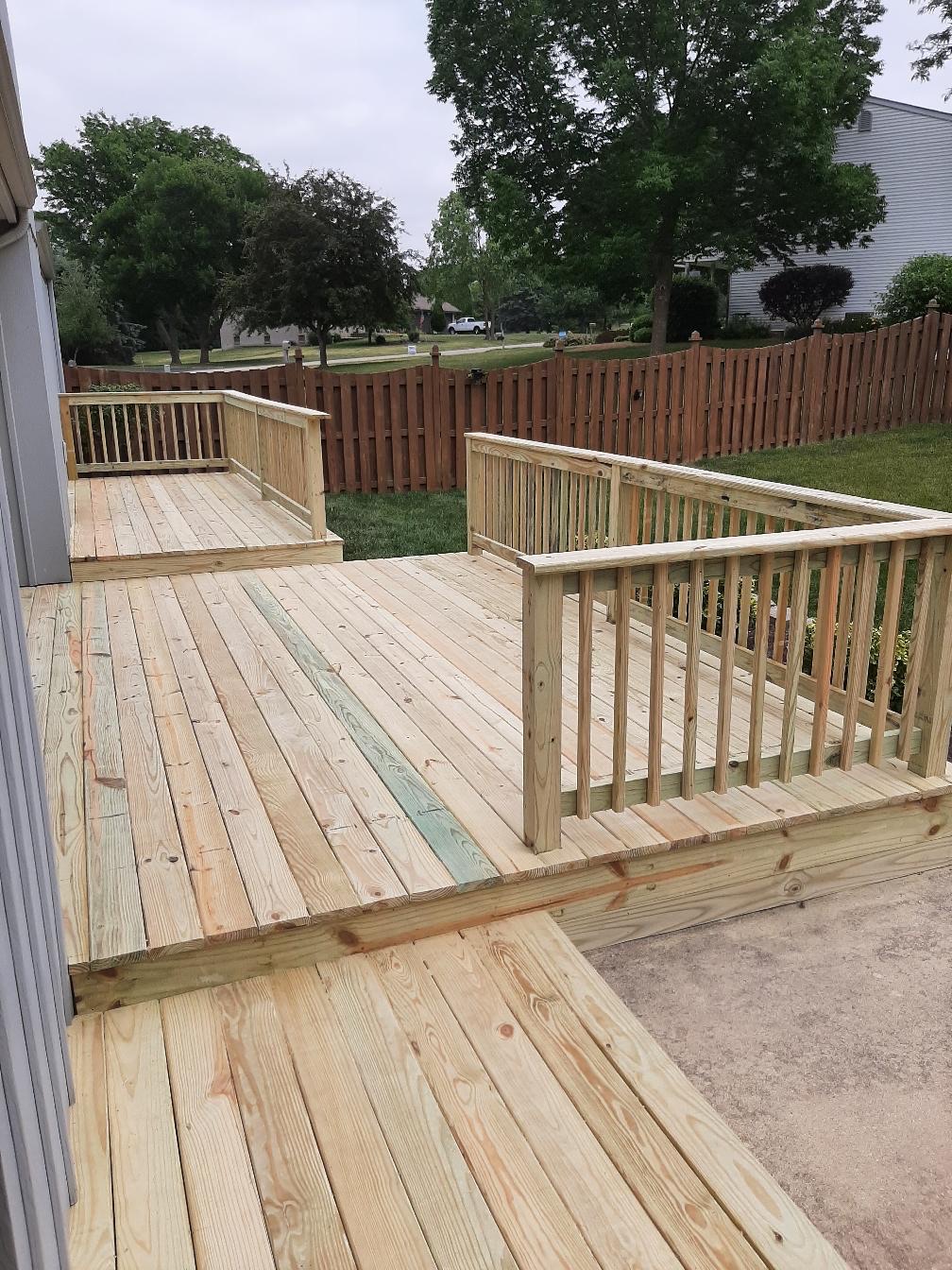 Multi-level custom residential pressure-treated wood deck with wood safety railings overlooking a fenced backyard, built by Precision Exterior Inc.