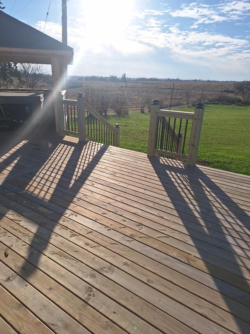 Custom residential wood deck with hybrid black metal spindle railings and a built-in staircase leading to a backyard lawn, constructed by Precision Exterior Inc.