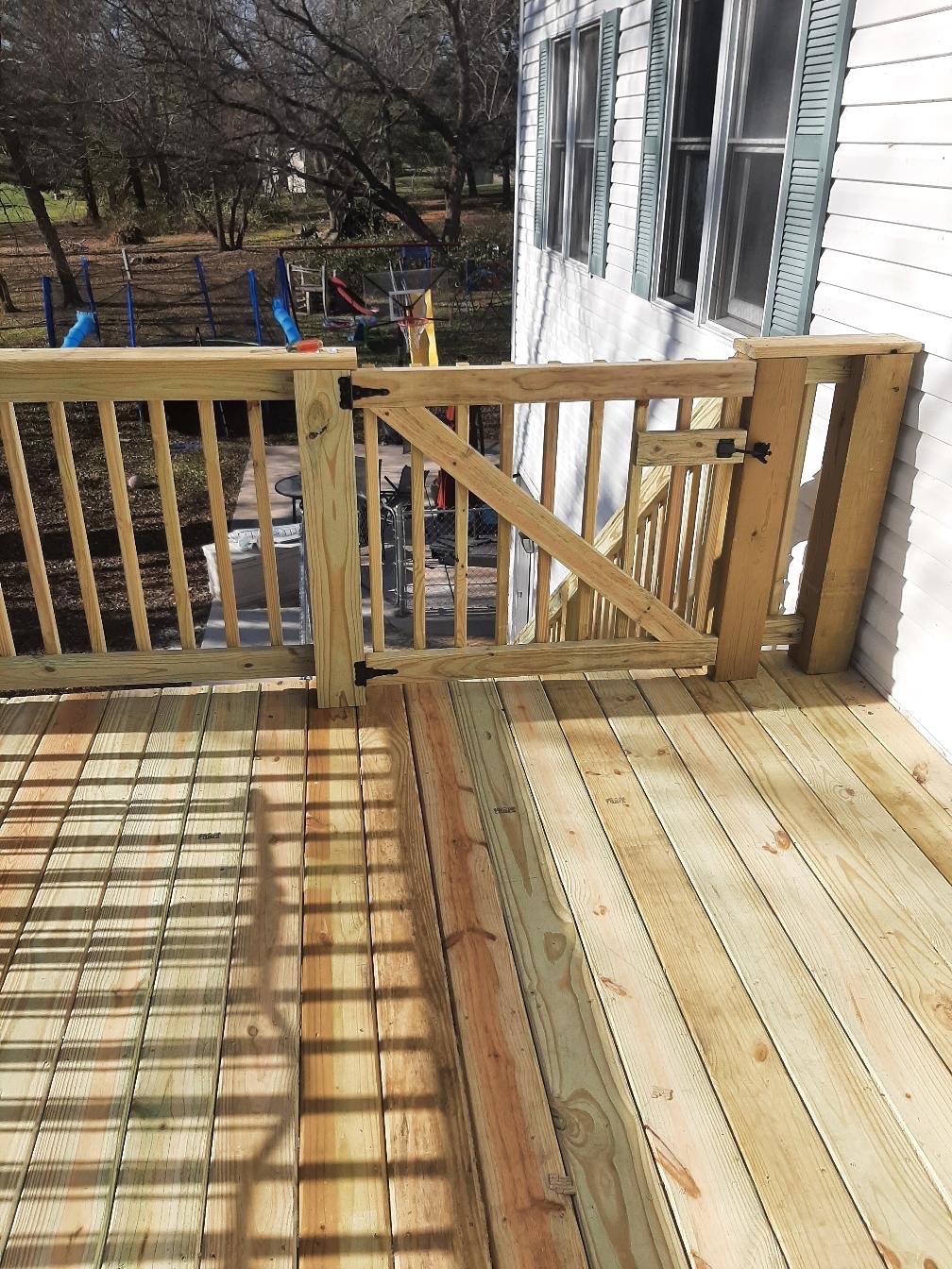 Custom pressure-treated wood deck safety gate and staircase railing installed on a residential house by Precision Exterior Inc.