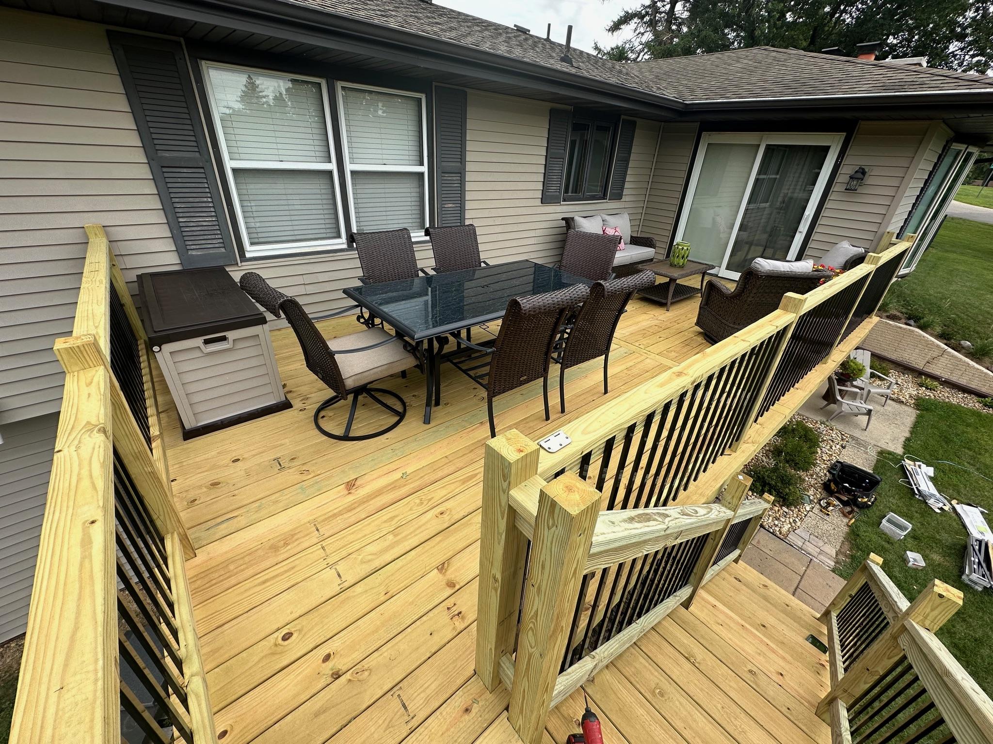 Custom wood deck with black metal baluster safety railings and outdoor patio furniture, built by Precision Exterior Inc. in Lena, IL.