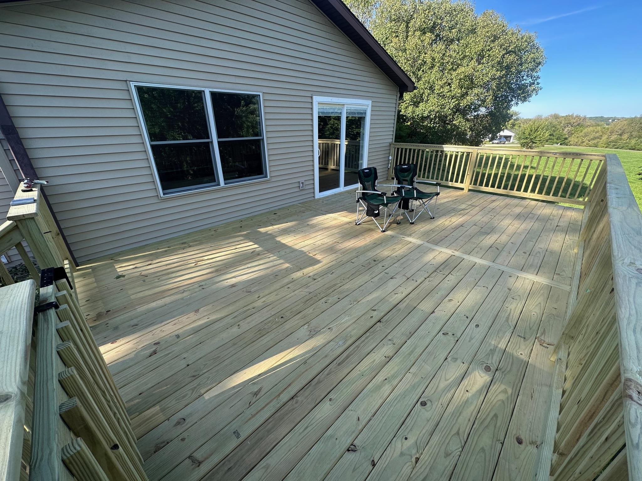 Custom pressure-treated wood deck with wooden safety railings built on a beige vinyl siding home by Precision Exterior Inc.