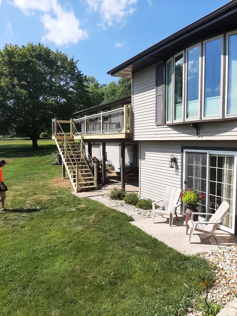 Custom elevated backyard wood deck with an attached staircase and black metal balustrade railings built on a split-level home by Precision Exterior Inc.