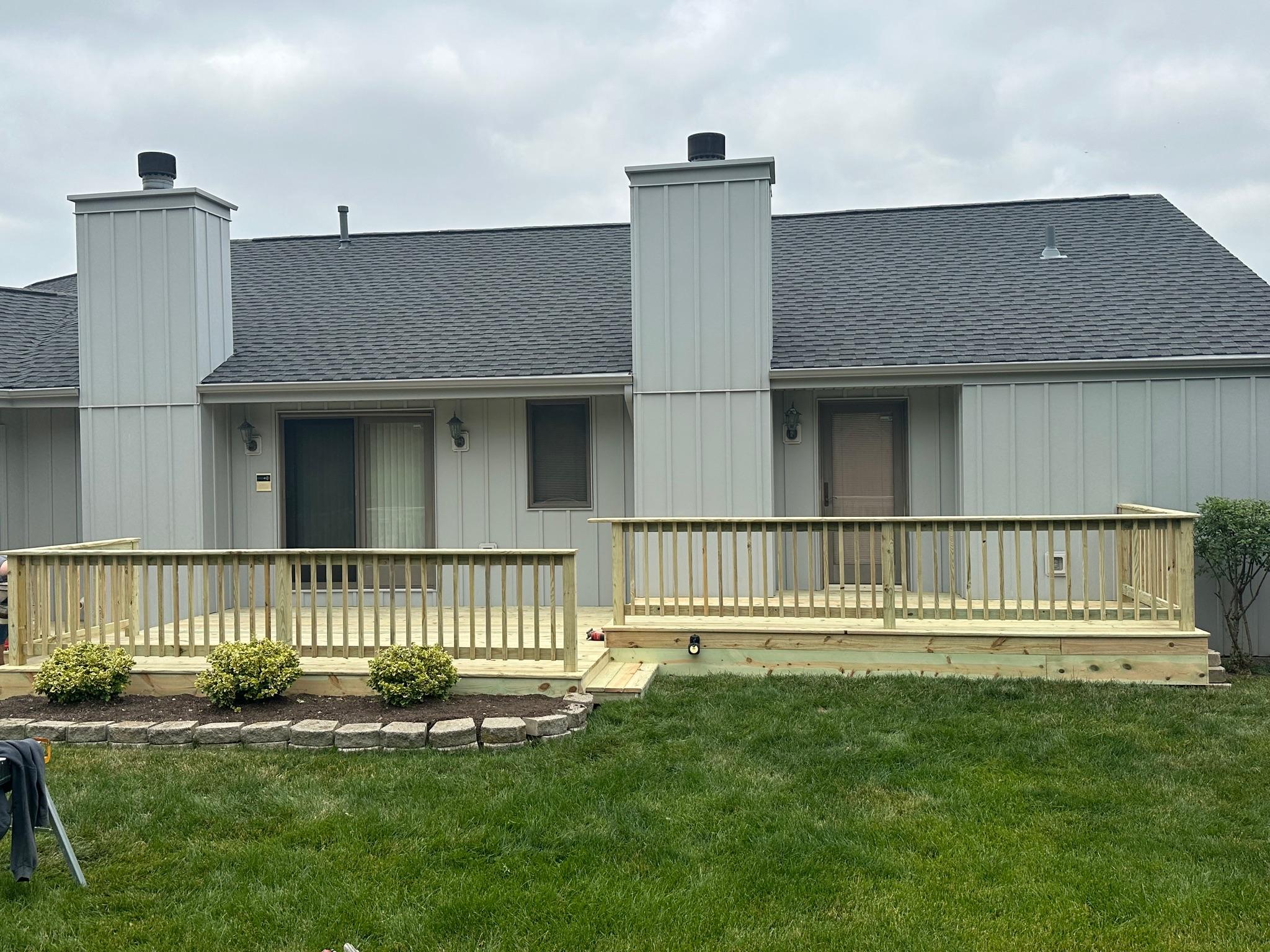 Multi-level backyard wooden patio deck with railings built on a grey siding house by Precision Exterior Inc.