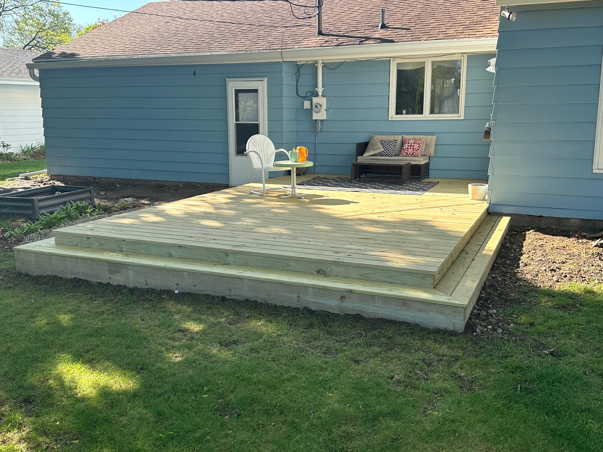 Ground-level pressure-treated wood patio deck with step-down stairs built on a blue vinyl siding home by Precision Exterior Inc.