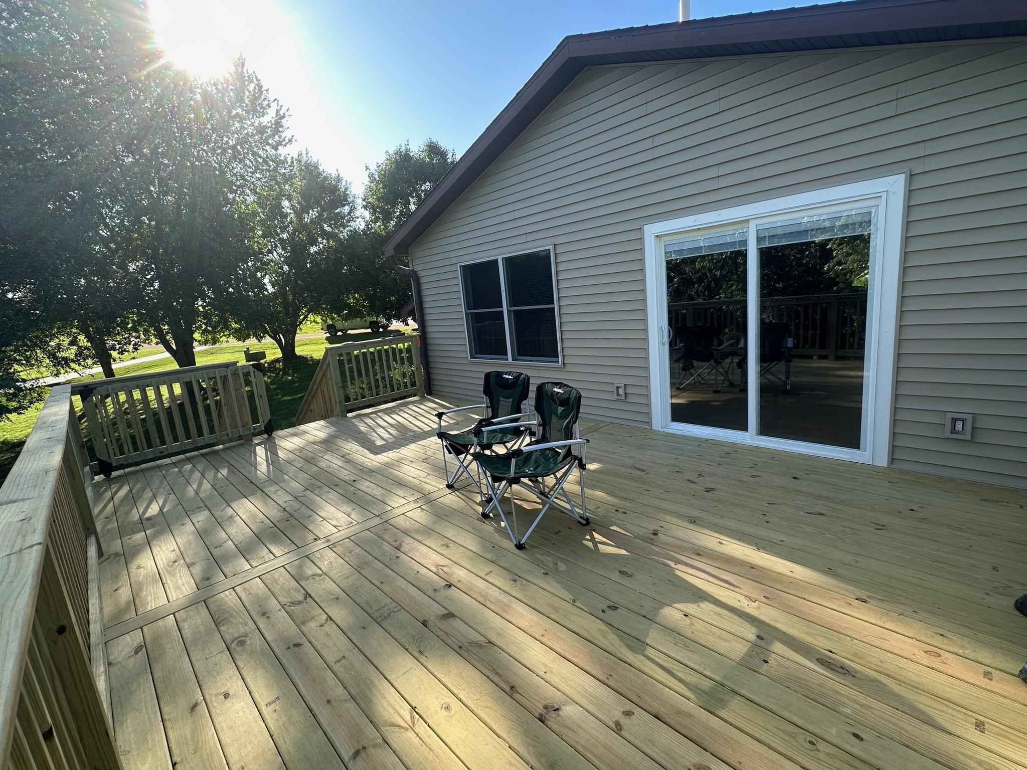Custom pressure-treated wooden backyard deck with railings and safety gate built on a beige vinyl siding home by Precision Exterior Inc.