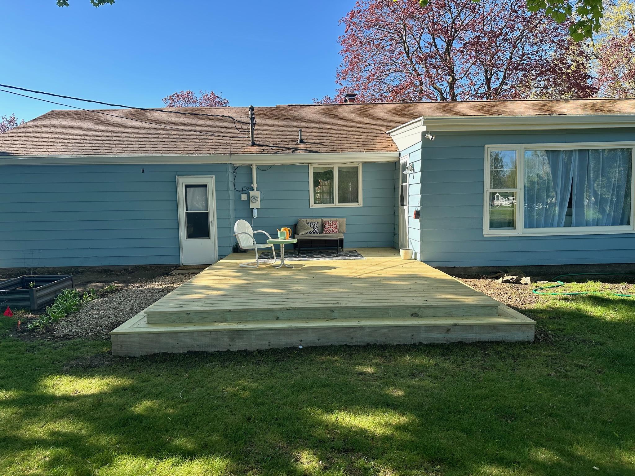 Custom ground-level pressure-treated wood platform deck built by Precision Exterior Inc. on a residential blue home in Lena, IL.