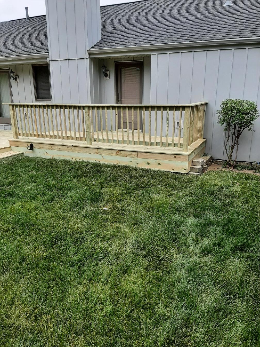 Custom pressure-treated wooden deck platform with safety railings built along a grey siding house by Precision Exterior Inc.