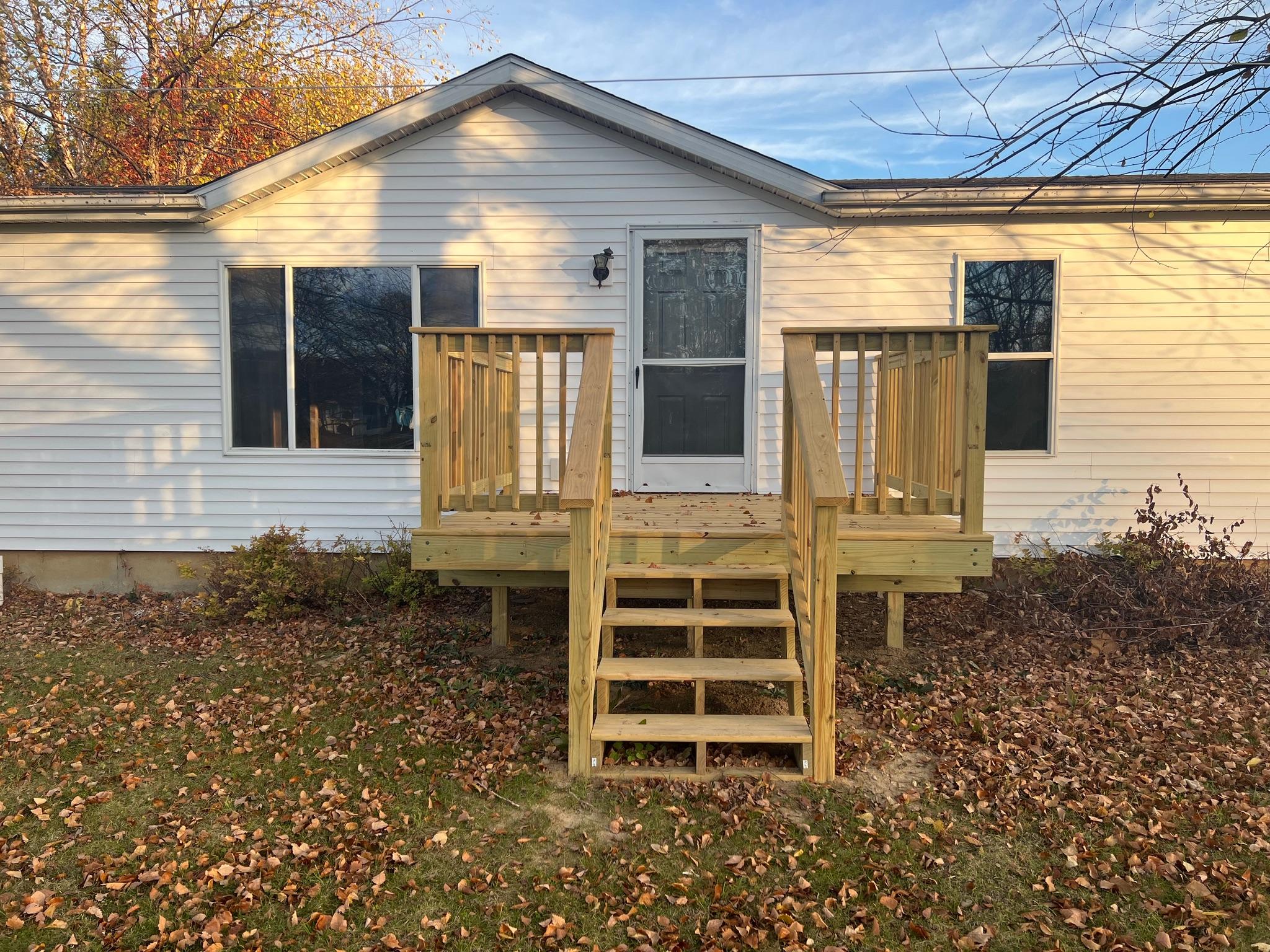 Custom wood front entry deck and steps built by Precision Exterior Inc. on a residential white home in Lena, IL.