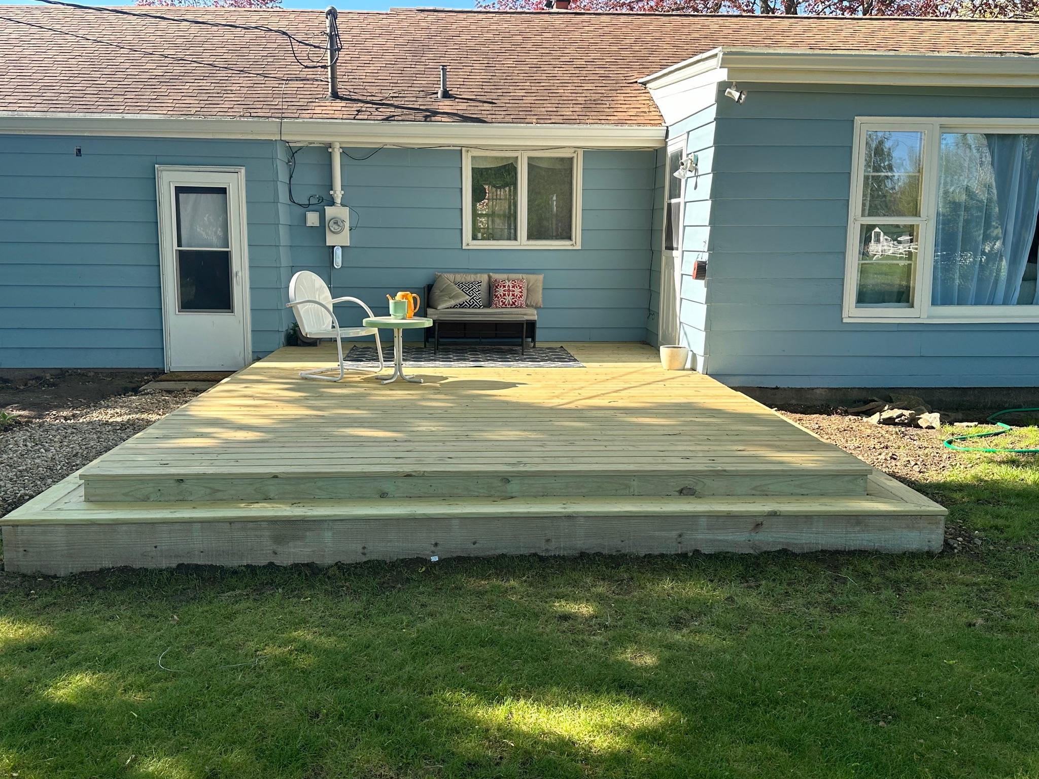 Custom ground-level pressure-treated wood deck with stairs built on a blue house by Precision Exterior Inc.