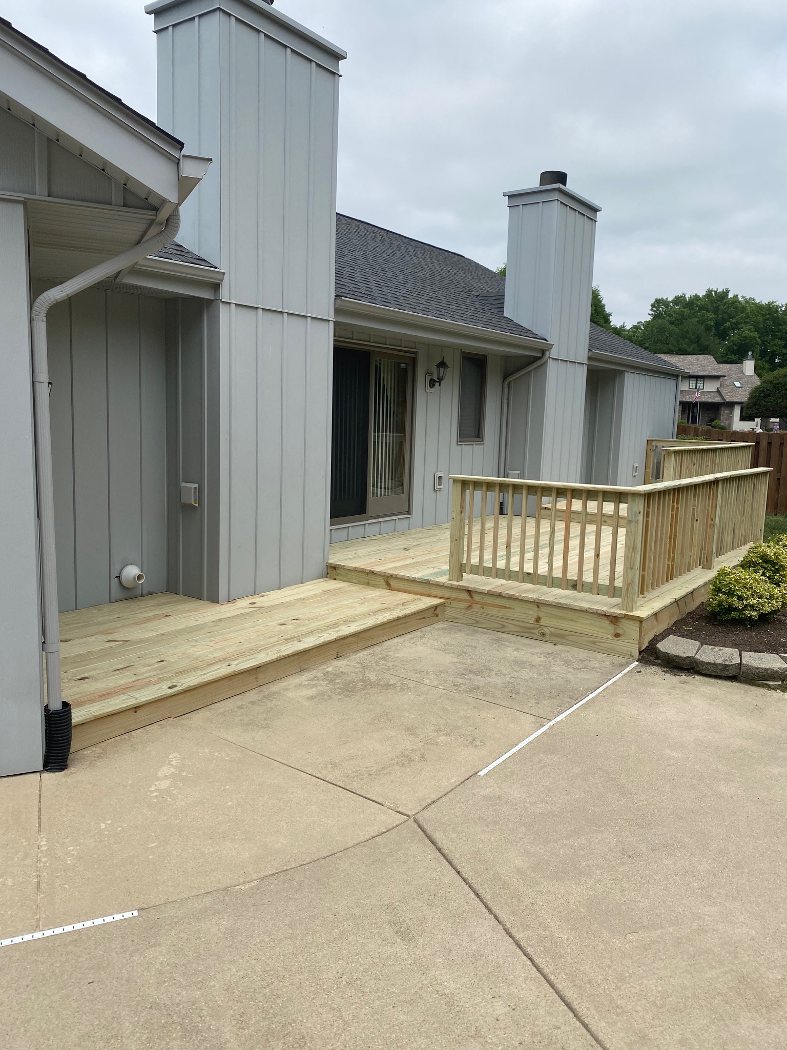 Multi-level backyard pressure-treated wood deck with wooden safety railings built alongside a concrete patio by Precision Exterior Inc.