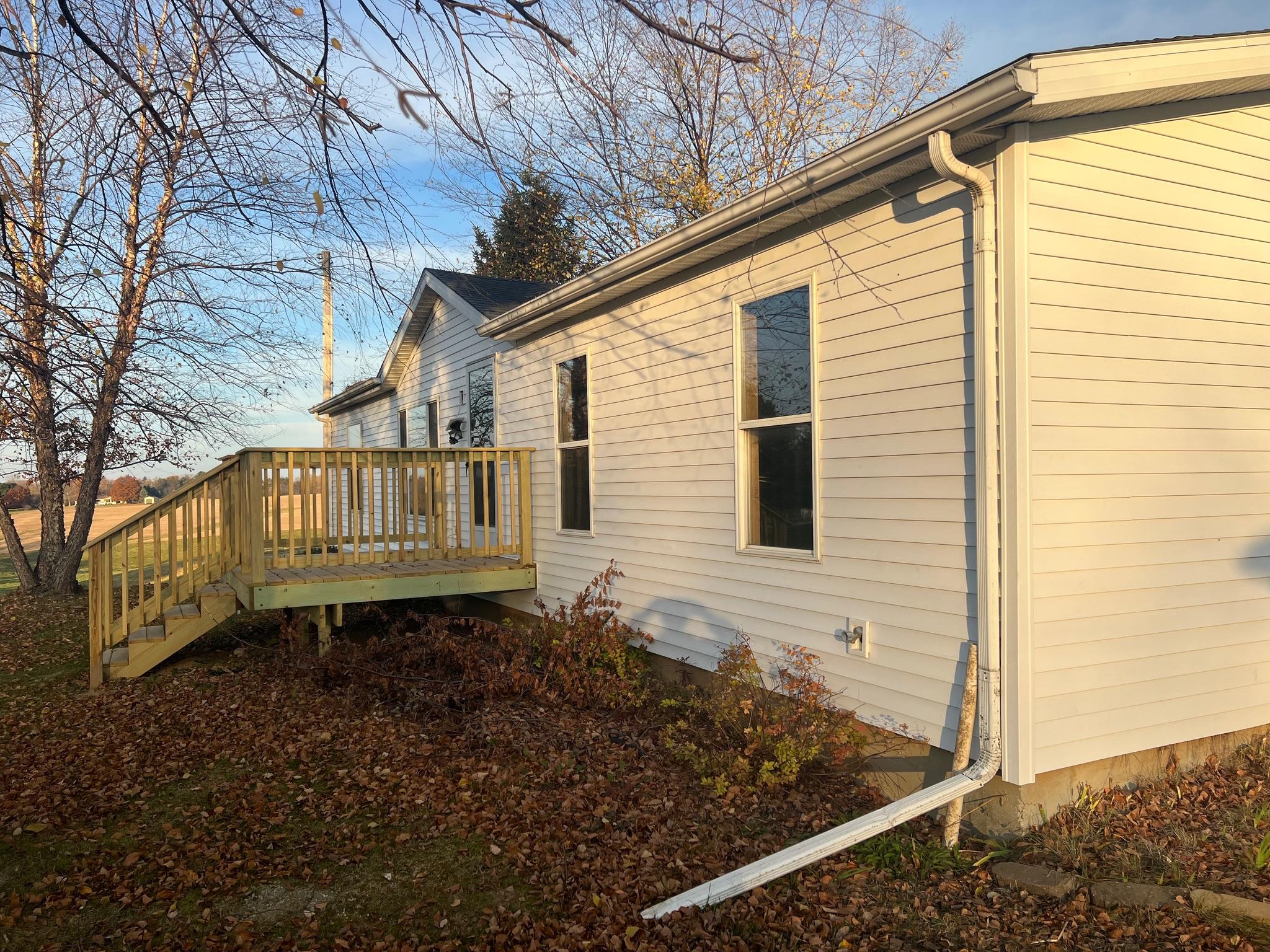 Custom wood porch deck and entry stairs installed on a white single-story house by Precision Exterior Inc. in Lena, IL.