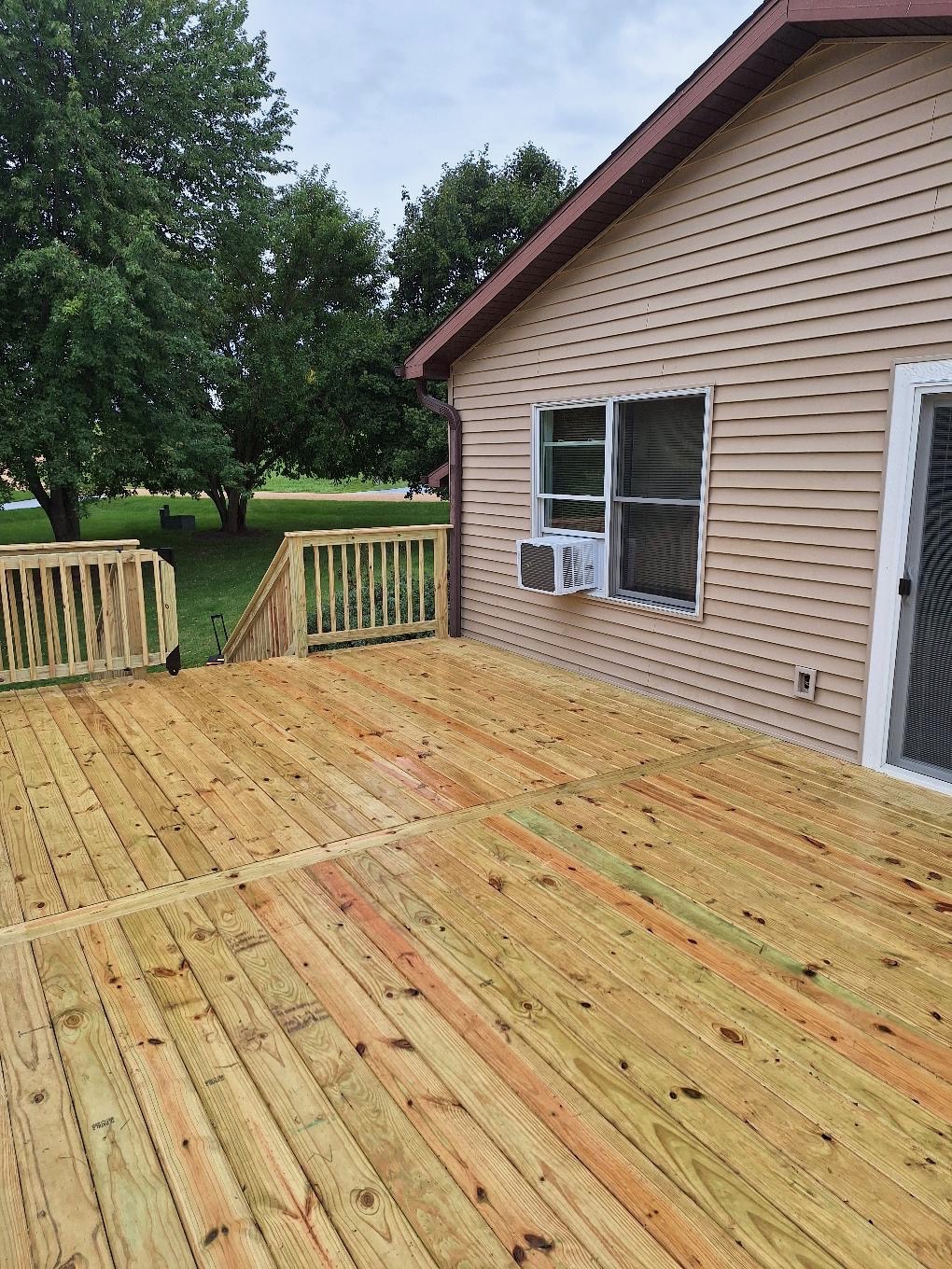 New pressure-treated wood deck boards, safety railings, and attached staircase built on a residential home by Precision Exterior Inc.