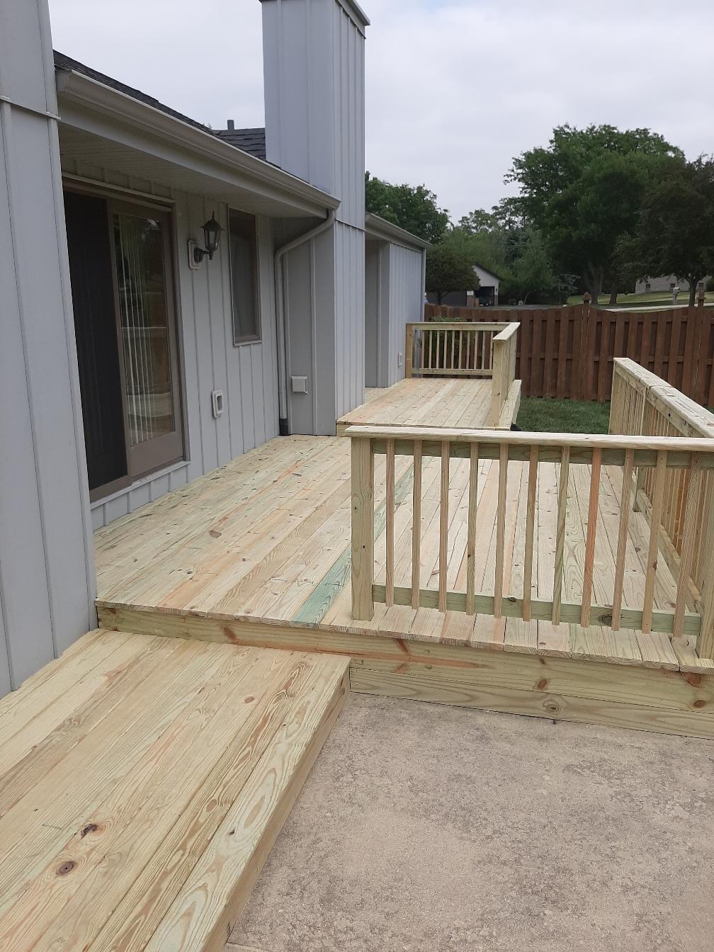 Custom multi-tier pressure-treated wood deck with secure wooden safety railings built along the back of a grey residential house by Precision Exterior Inc.