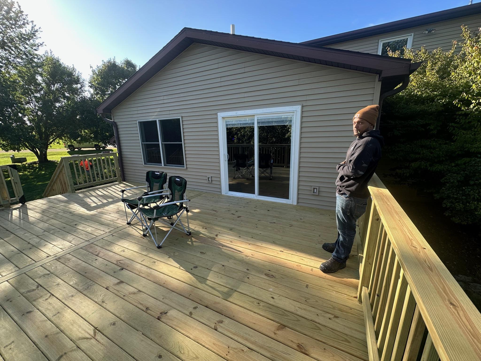 Custom pressure-treated wooden deck with railings built on a beige vinyl siding house by Precision Exterior Inc.