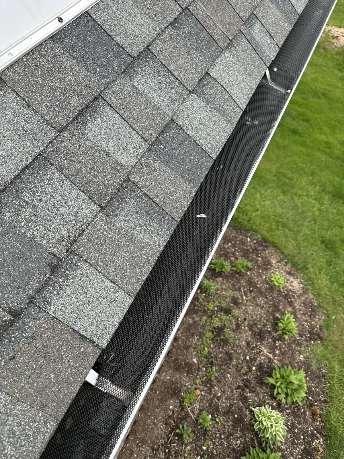 A close-up view of a functional white gutter system on a home with tan siding, a service provided by Precision Exterior Inc.