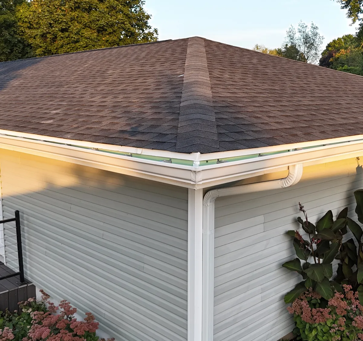 A close-up view of a functional white gutter system on a home with tan siding, a service provided by Precision Exterior Inc.