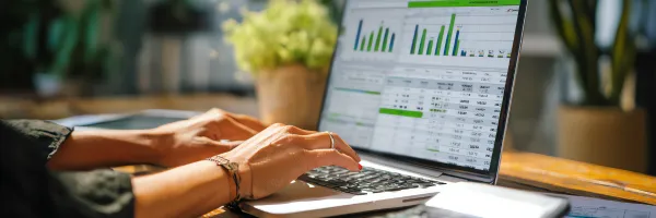 Close up of hand on a computer with financial graphs on the screen.