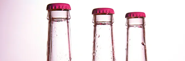 Tops of three bottles in a row on a light pink background with pink metal lids.