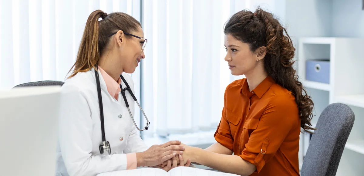 Doctor comforting patient by holding hand in office at an appointment