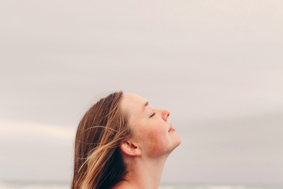 Donna di profilo in riva al mare che respira con il viso disteso verso l'alto — calma e regolazione del sistema nervoso.