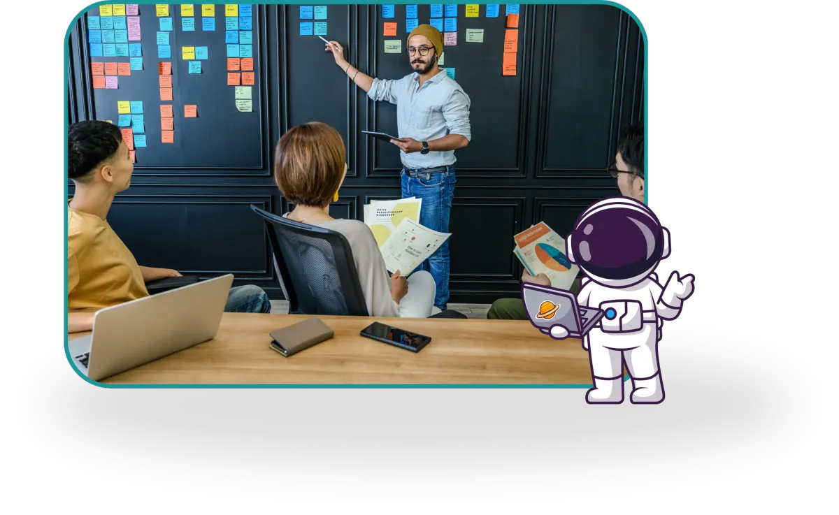 A man stands by a wall of colorful sticky notes, presenting to three seated colleagues in a modern office. 