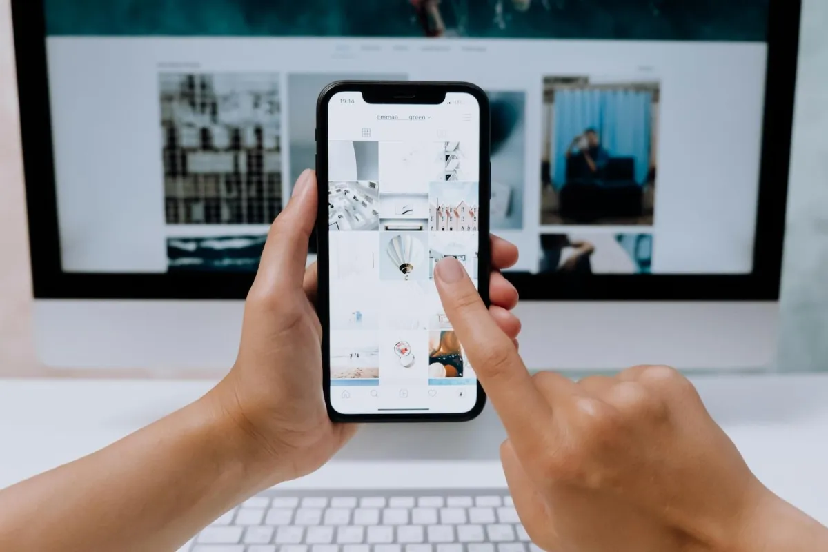 Phone screen showing an Instagram grid held infront of a desktop computer