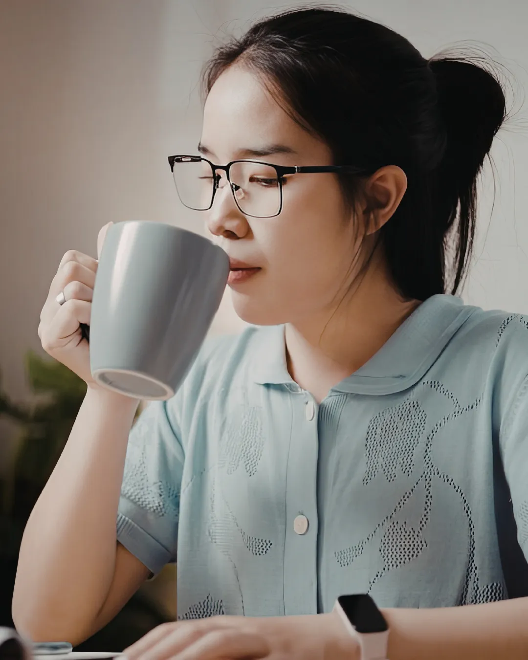 Woman wearing glasses drinking coffee at home while working on laptop