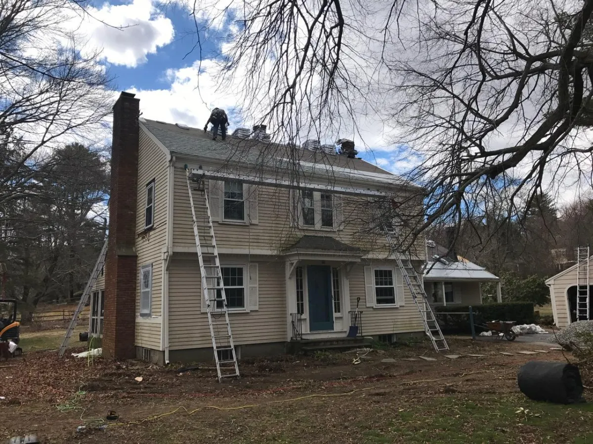Roof replacement in progress by McCarthy Exteriors LLC on a two-story home in New Hampshire with winter conditions