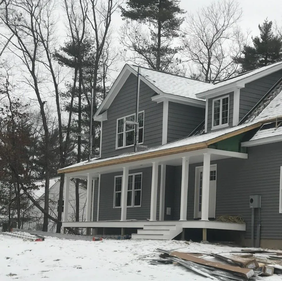 New construction home with gray siding during snowy conditions in New Hampshire by McCarthy Exteriors LLC