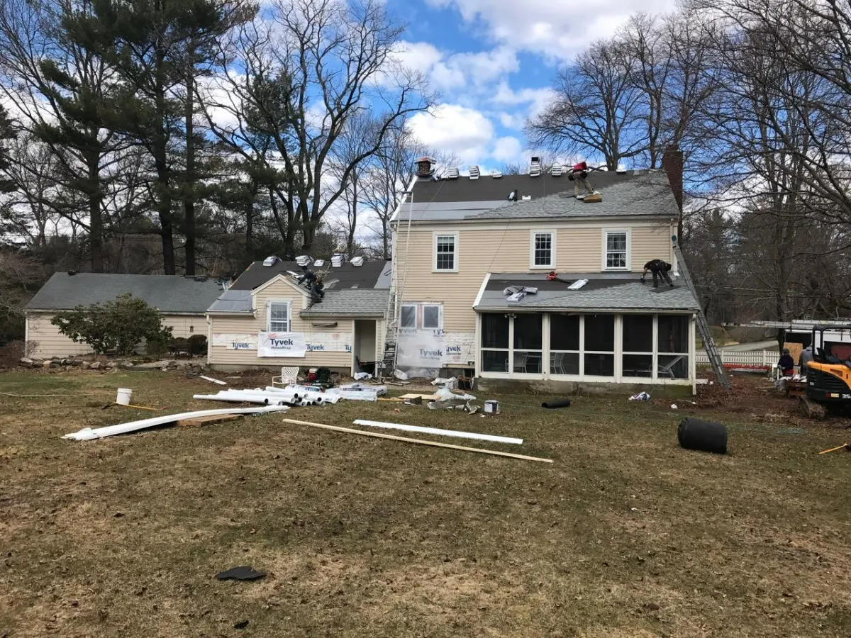 Roof replacement project in progress on a two-story house with roofing materials and equipment on the ground
