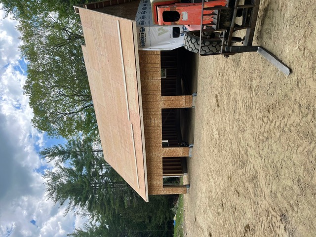 Roof replacement project in progress on a two-story house with roofing materials and equipment on the ground