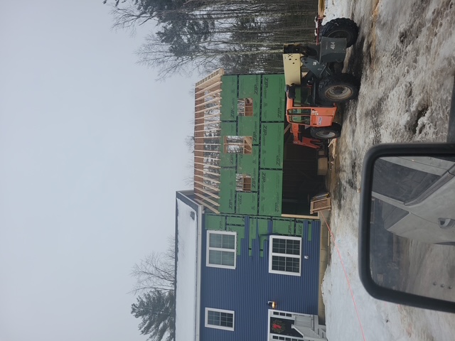 Roof replacement project in progress on a two-story house with roofing materials and equipment on the ground