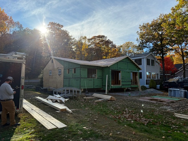 Two-story house undergoing roof repairs with ladders positioned along the roofline and workers on the roof