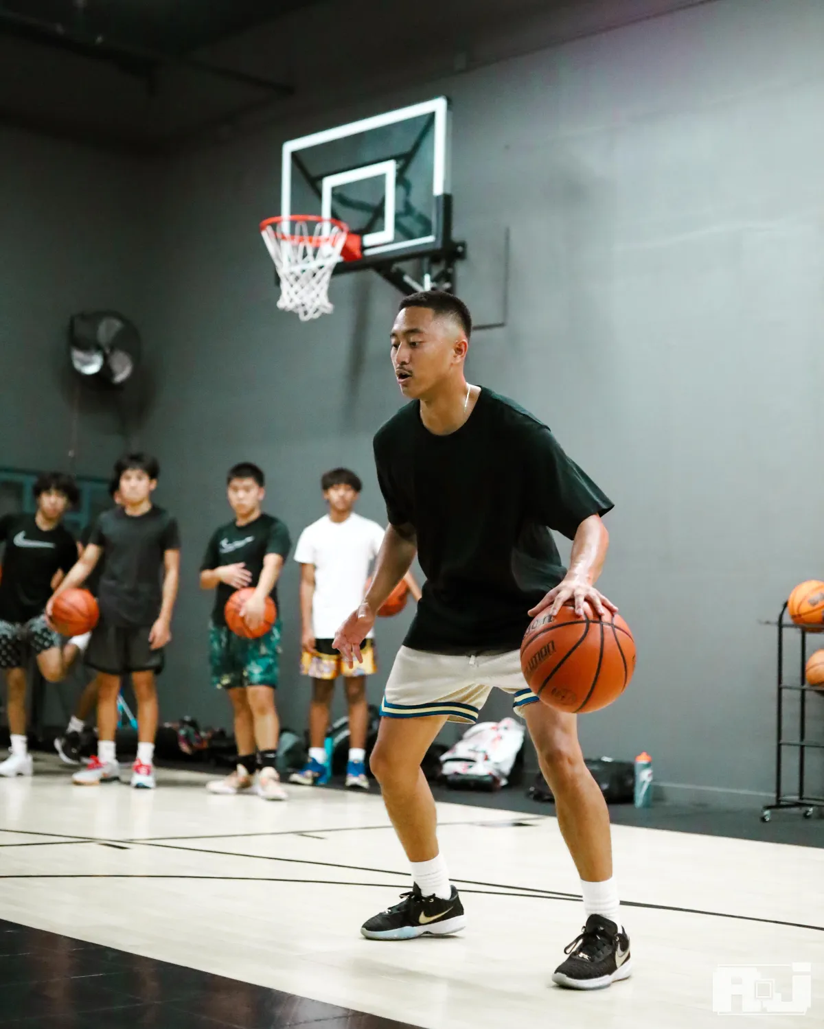 Basketball trainer Elijah Deguzman on a court during a training session, dribbling and demonstrating and engaging with athletes, showcasing a professional basketball training environment.