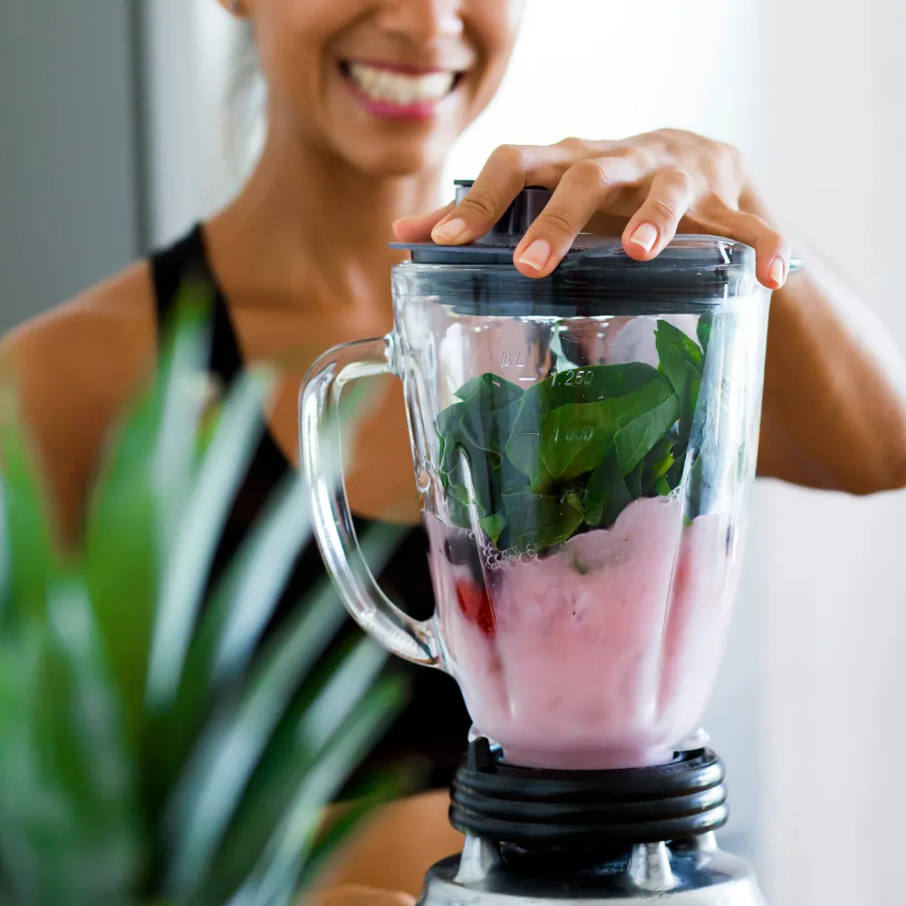 A smiling woman holds a blender, ready to prepare a smoothie or meal
