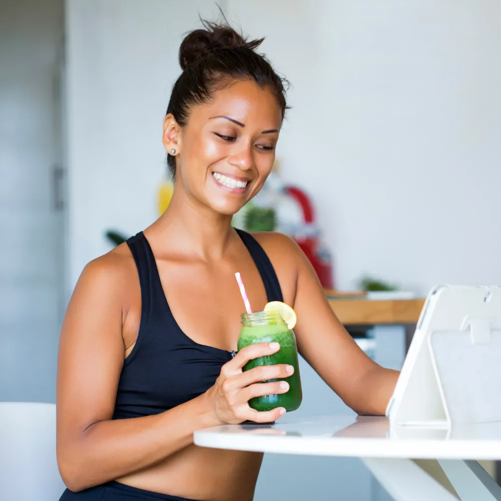 A fit woman wearing a black sports bra is holding a green smoothie