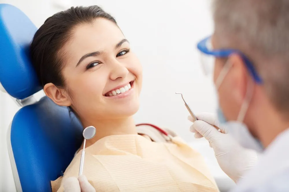 female dental professional smiling wearing white lab coat and gloves