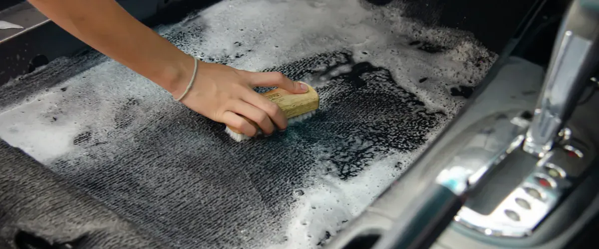 Hand scrubbing a car's interior carpet during deep cleaning.