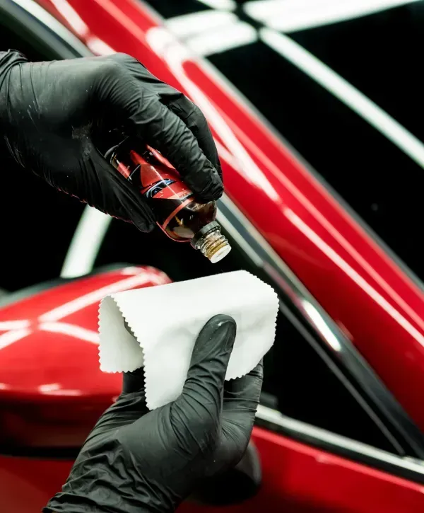 Applying ceramic coating to a red car using a microfiber cloth and dropper bottle