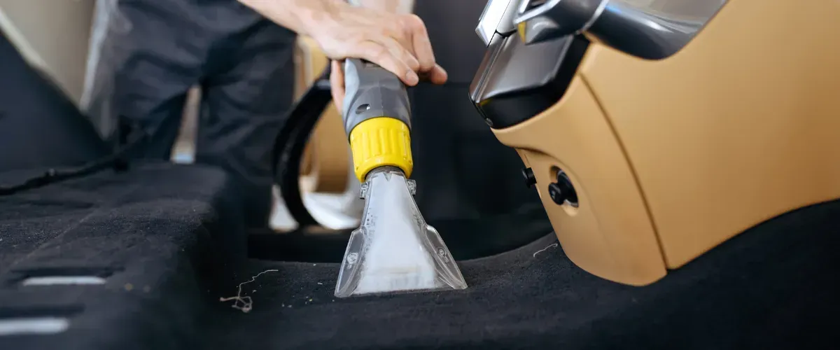 Hand scrubbing a car's interior carpet during deep cleaning.