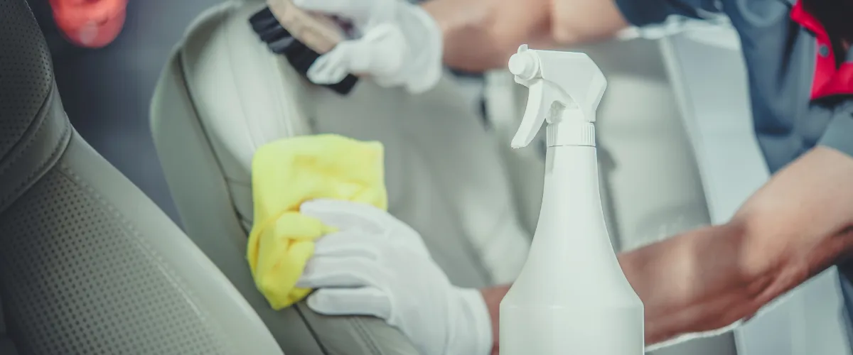 Detailing professional cleaning leather car seats with spray bottle and cloth"  auto-detailing-expert-cleaning-car-interior.webp