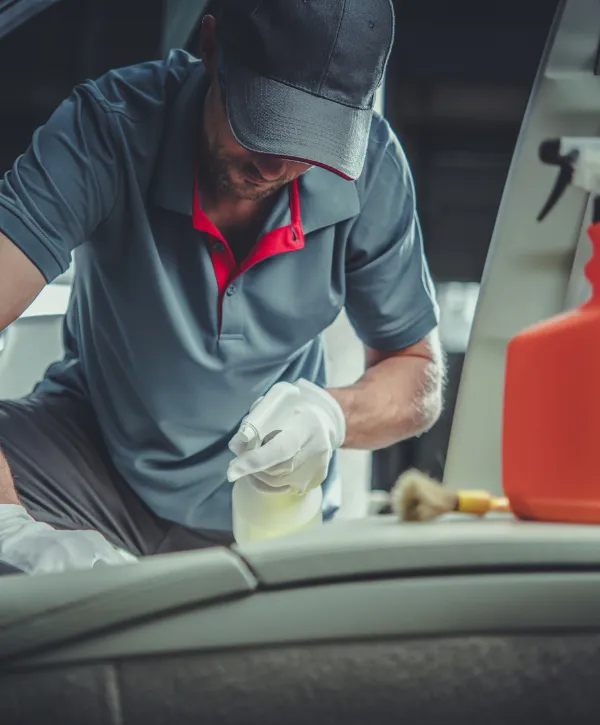 Auto detailing expert cleaning car interior with spray bottle and brush