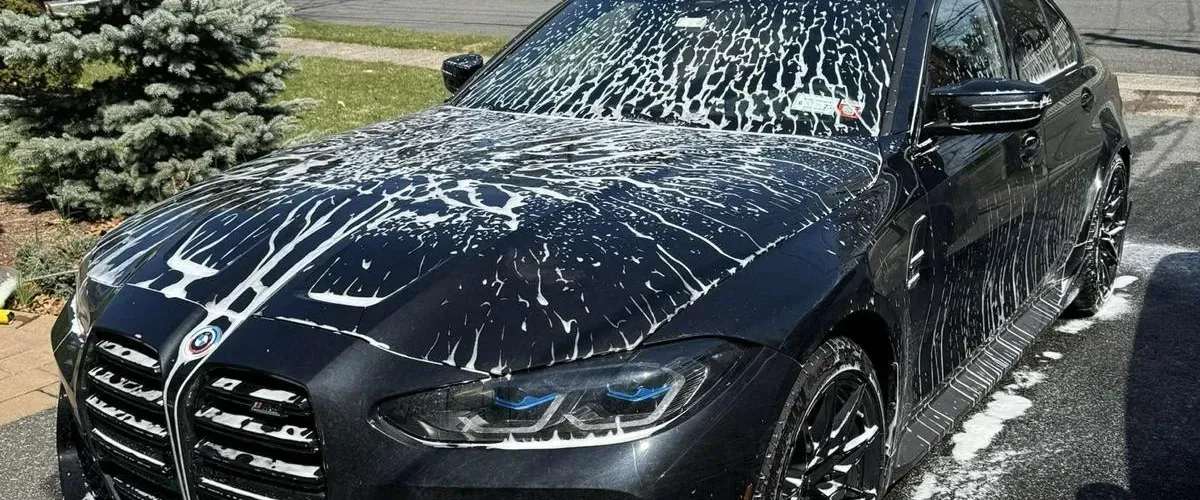 Black BMW sedan covered in white foam during an exterior car wash and detailing session.