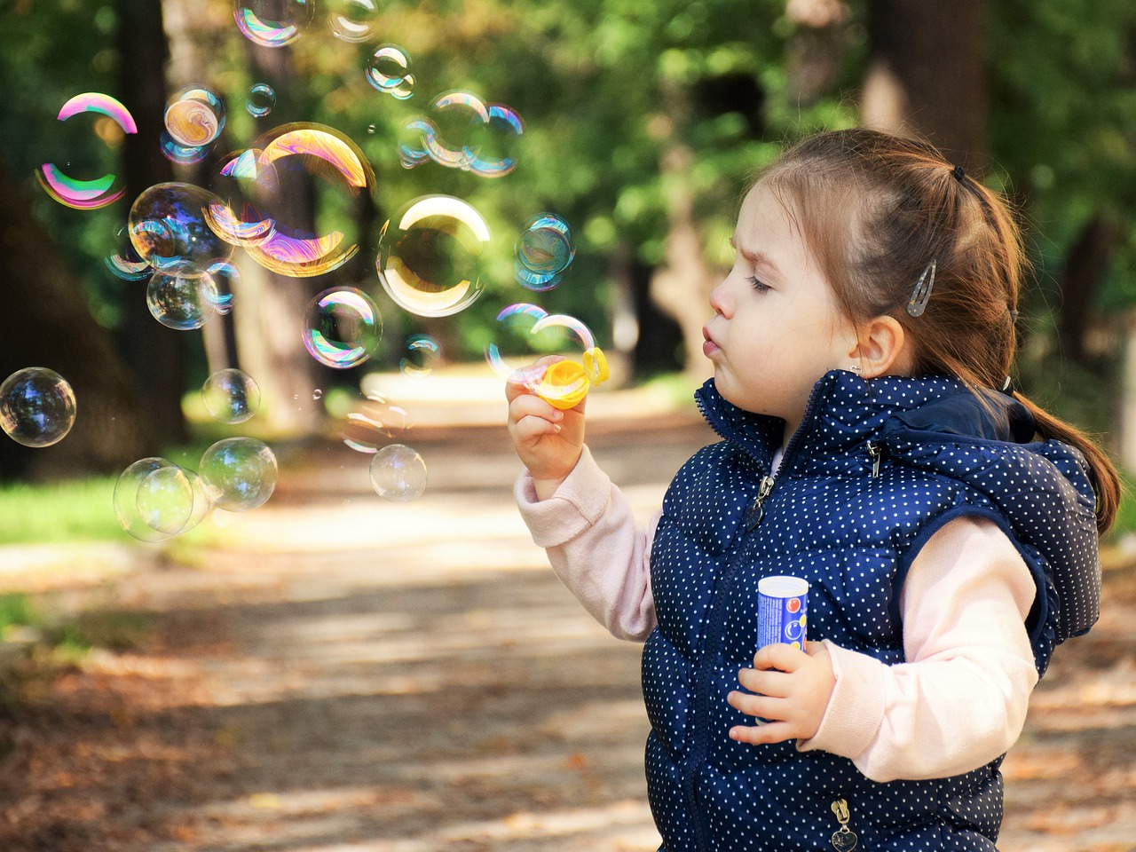 little girl blowing bubbles at a park 